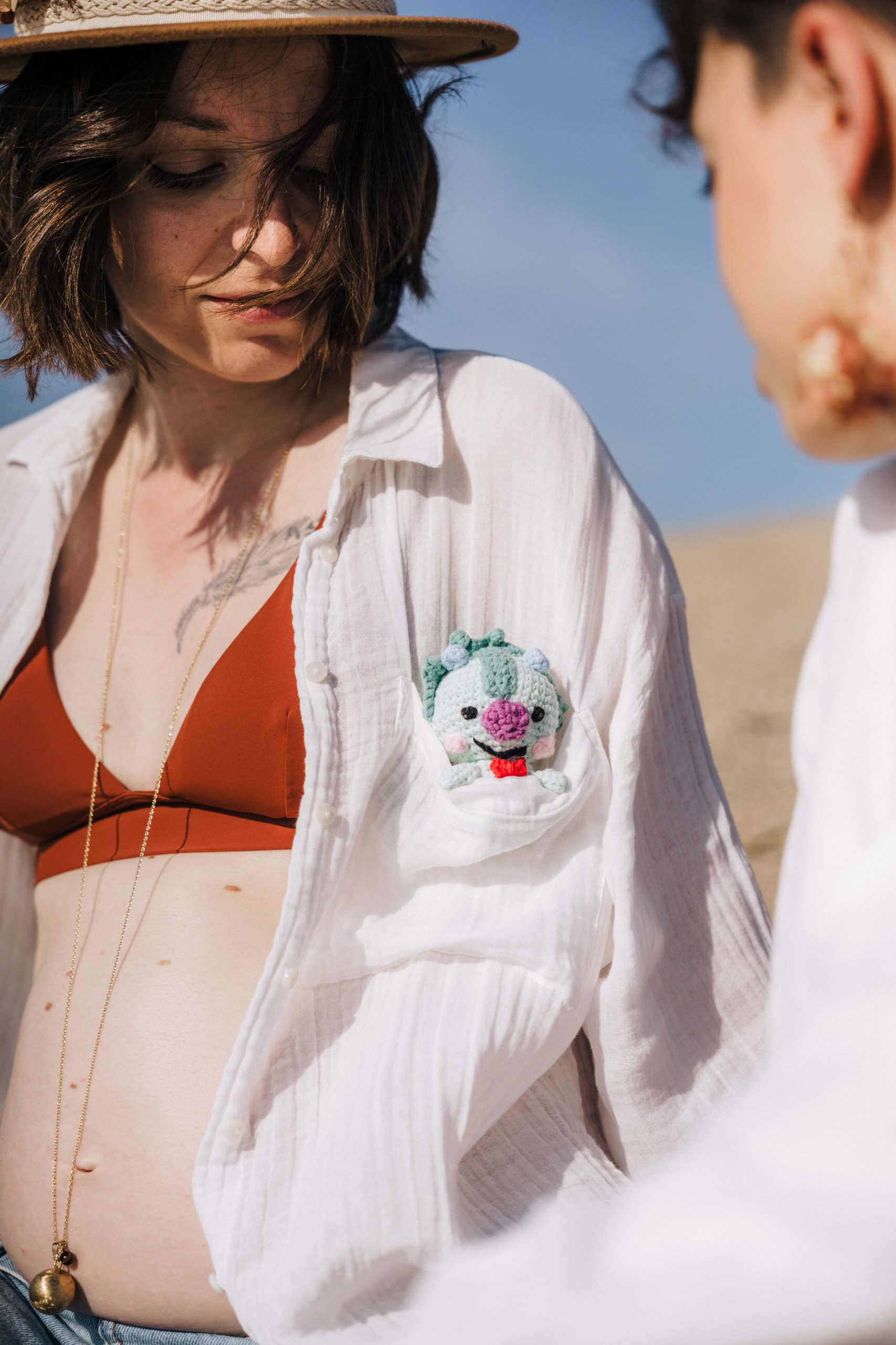 Gros plan sur Nelly, le ventre de grossesse apparent, avec une petite peluche de dinosaure en crochet dans la poche de sa chemise, lors de sa séance à Argelès-sur-Mer.